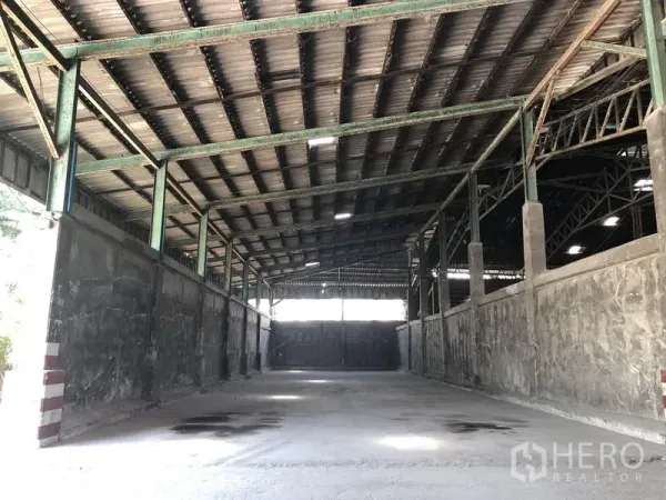 Warehouse for rent in Thanyaburi, Pathum Thani - Enclosed storage bay under a metal roof with tall side walls and a sliding door at the end.