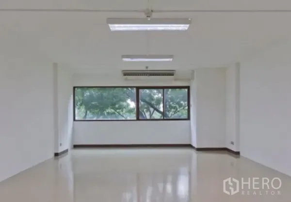 Office Space for rent in Chatuchak, Bangkok - Bright empty office room with large window, tree views, ceiling fluorescent lights and wall-mounted air conditioner.