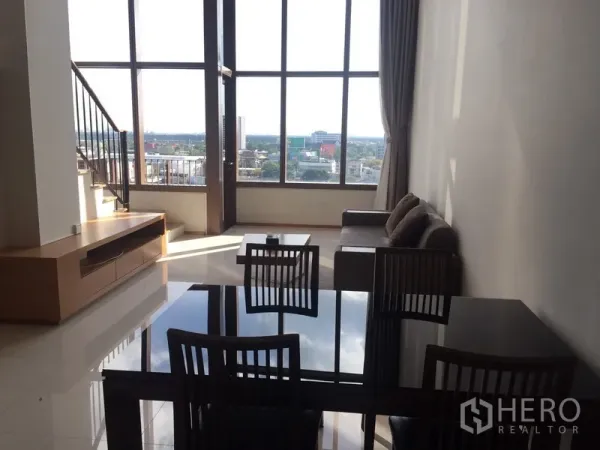 Condominium for rent in Khlong Toei, Bangkok - Open living and dining area with high ceilings, floor-to-ceiling windows, staircase and city views.