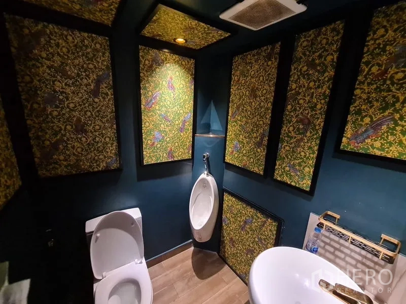 Retail Space for rent in Bang Rak, Bangkok - Restroom with decorative patterned panels, toilet and urinal under warm lights.