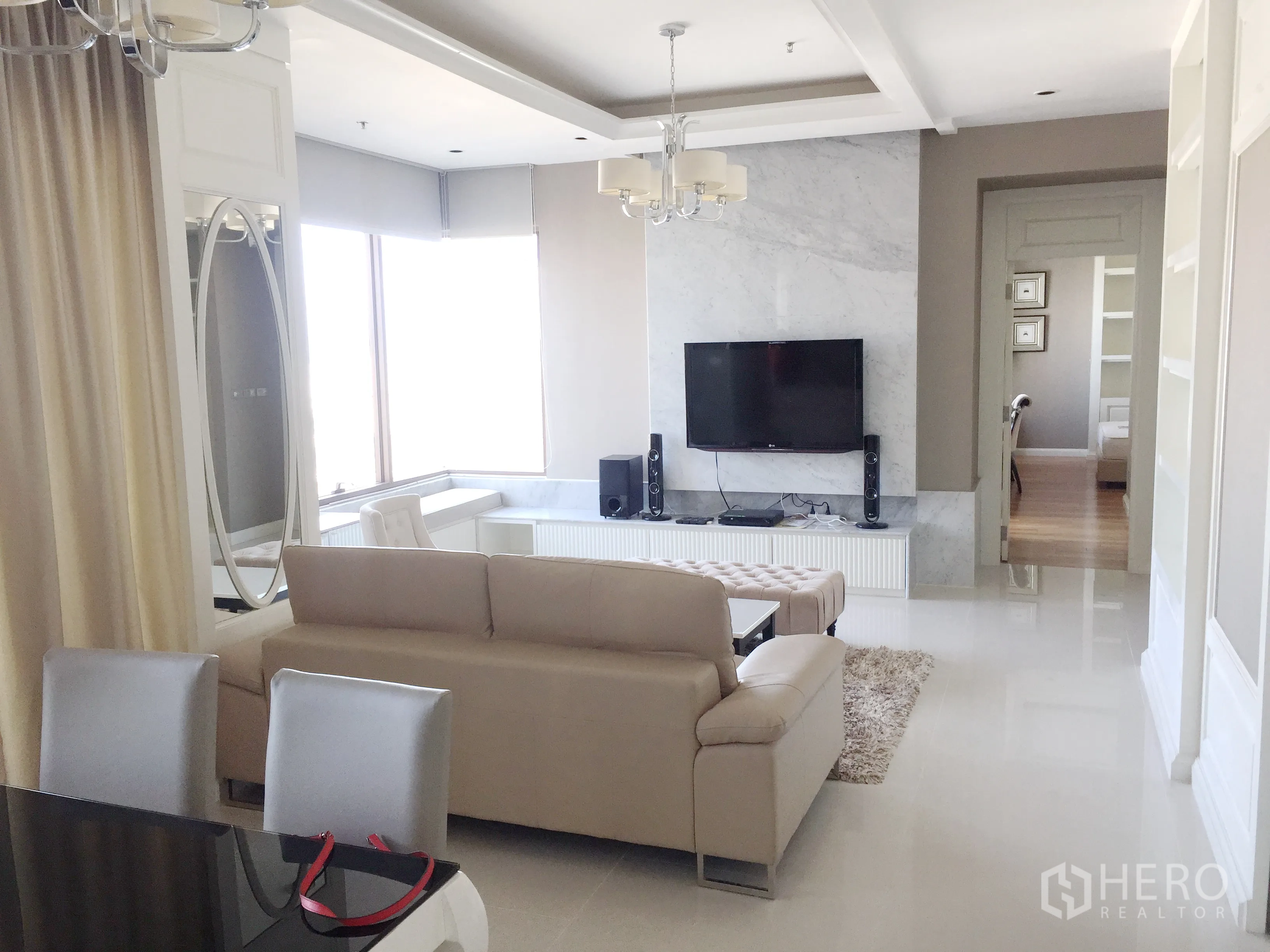 Condominium for rent in Khlong Toei, Bangkok - Open-plan living and dining room with beige sofa, TV on marble feature wall and chandelier lighting.