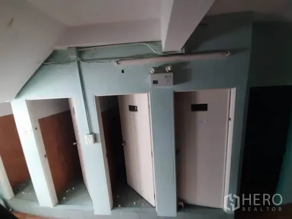 Shophouse for rent in Watthana, Bangkok - Row of restroom cubicles with white doors under a stairwell and tiled flooring.