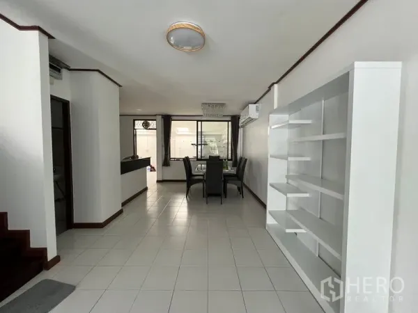Townhouse for rent in Din Daeng, Bangkok - Open-plan living and dining area with white tile floors, staircase and built-in shelving.