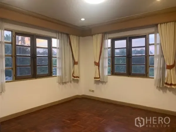 Detached House for rent in Khan Na Yao, Bangkok - Bright corner bedroom with multiple wooden-framed windows, drapes, and parquet floor.