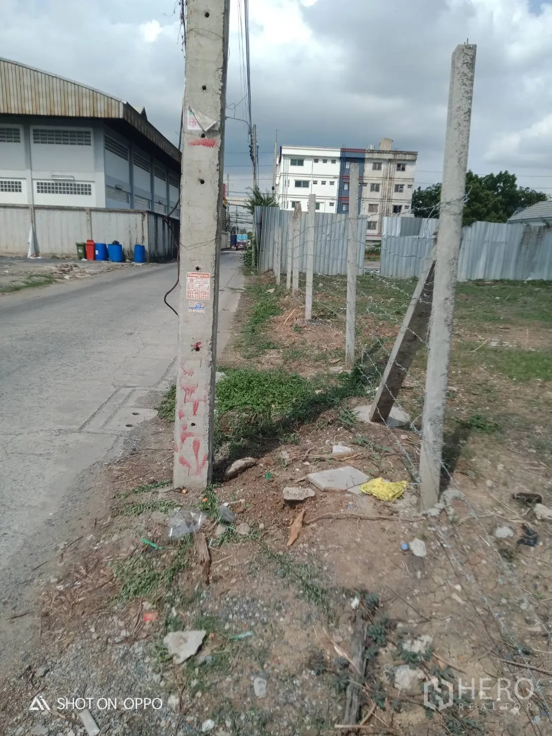 地 出租在Khan Na Yao, Bangkok - 地块拐角与电线杆，设有铁丝网立柱，左侧为仓库建筑。