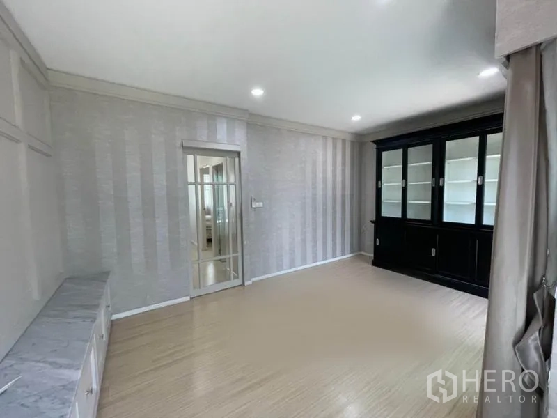 Townhouse for sale in Suan Luang, Bangkok - Spacious living room with glass-front display cabinet and balcony access via sliding door.