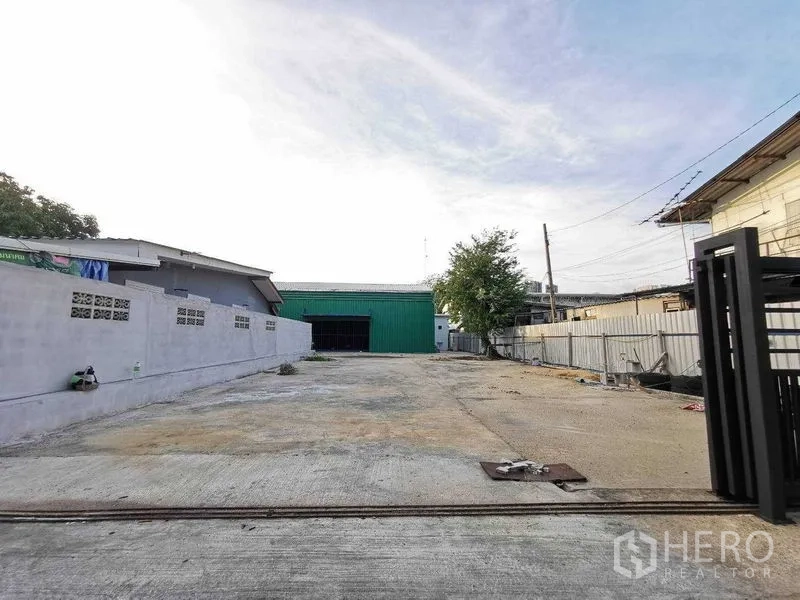Warehouse for rent in Bang Na, Bangkok - Wide concrete driveway leading to a green metal warehouse and open yard