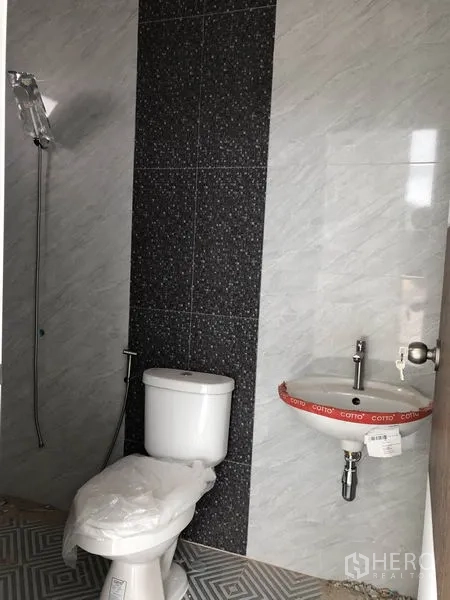 Factory for rent or sale in Sai Noi, Nonthaburi - Newly installed bathroom with wall tiles, toilet, handheld shower and compact sink.