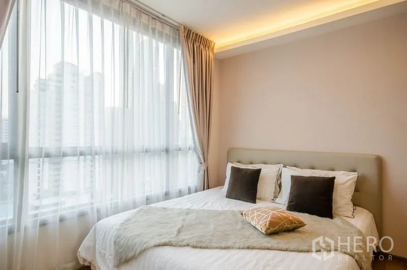 Condominium for rent or sale in Watthana, Bangkok - Bedroom with large corner windows, sheer curtains and a city view.