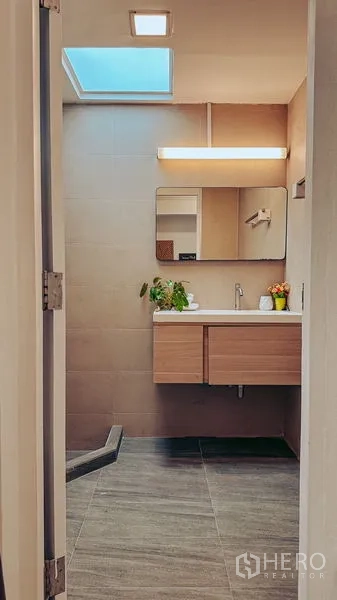Home Office for rent in Watthana, Bangkok - Modern bathroom with skylight, wood vanity, mirror, and neutral tiles.