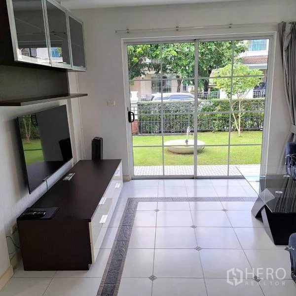 Detached House for rent in Prawet, Bangkok - Living room with TV console and wide sliding glass doors opening to the garden.