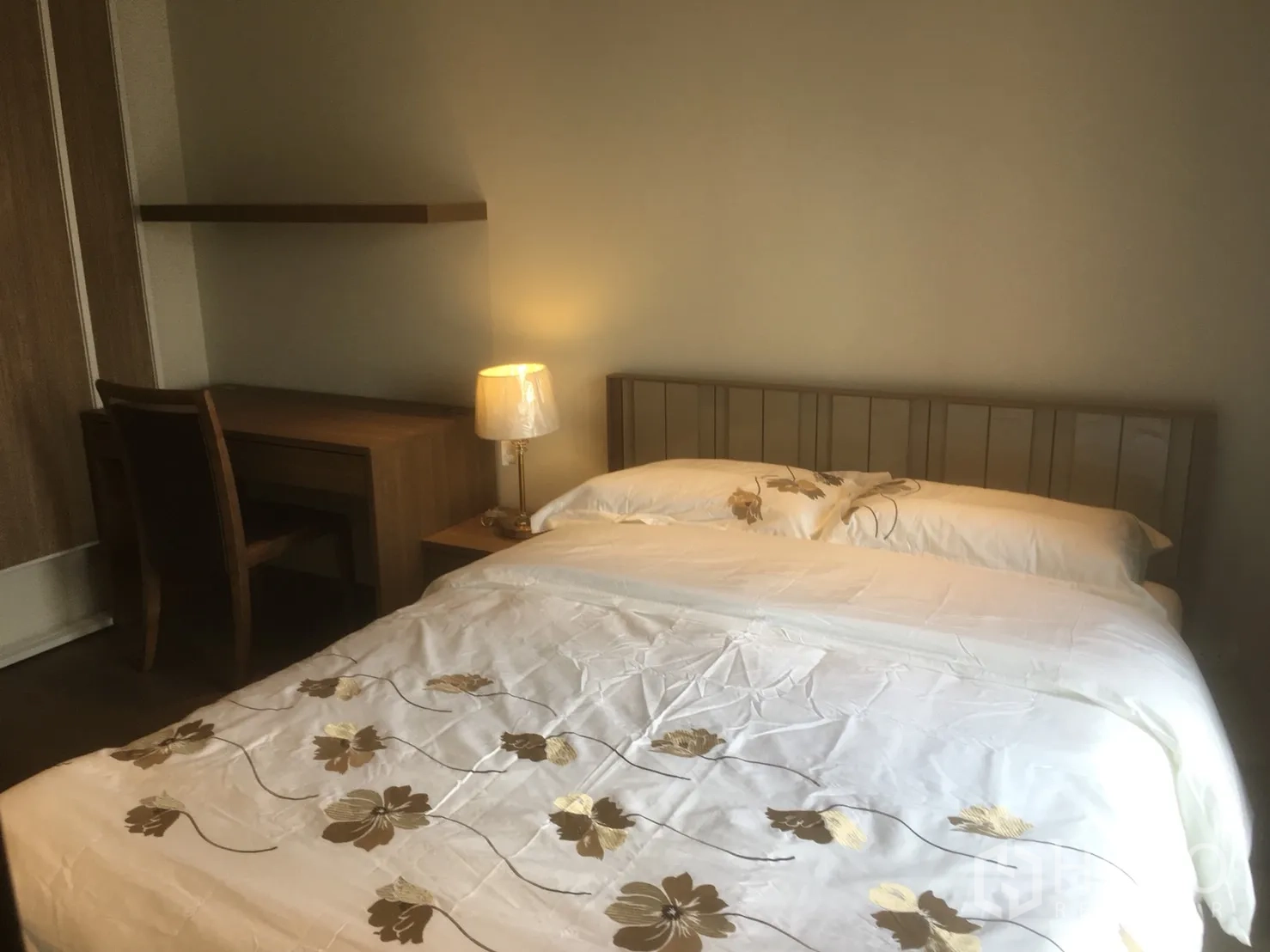 Condominium for rent or sale in Khlong Toei, Bangkok - Cozy bedroom close-up with floral duvet, wooden desk and warm bedside lamp.