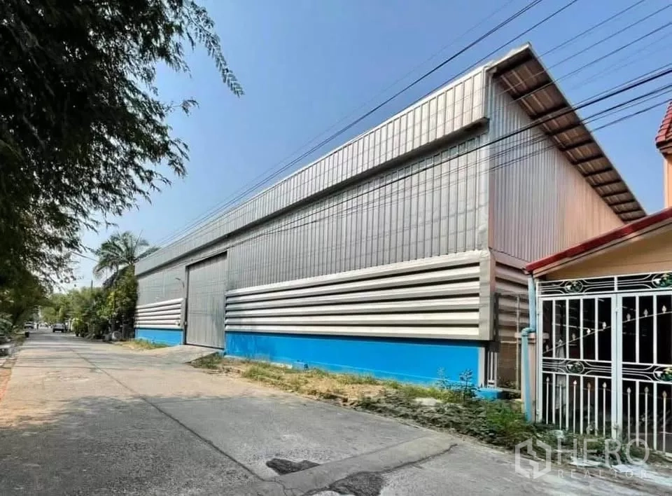 Warehouse for rent in Thanyaburi, Pathum Thani - Street view of a metal-clad warehouse with high gable roof and wide roller door in Thanyaburi, Pathum Thani.