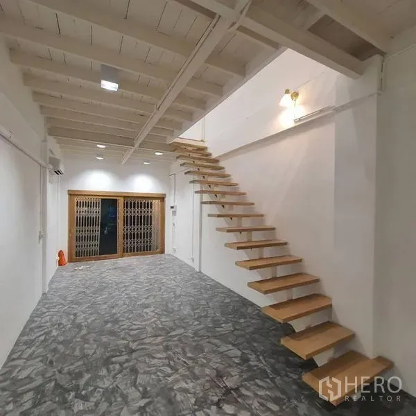 Shophouse for rent or sale in Khlong Toei, Bangkok - Open-plan ground floor with polished concrete floor and a floating wooden staircase.