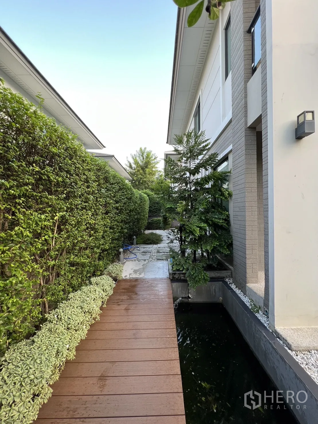 独立式住宅 出租在Suan Luang, Bangkok - 侧边步道，木桥沿锦鲤池与修剪绿篱。
