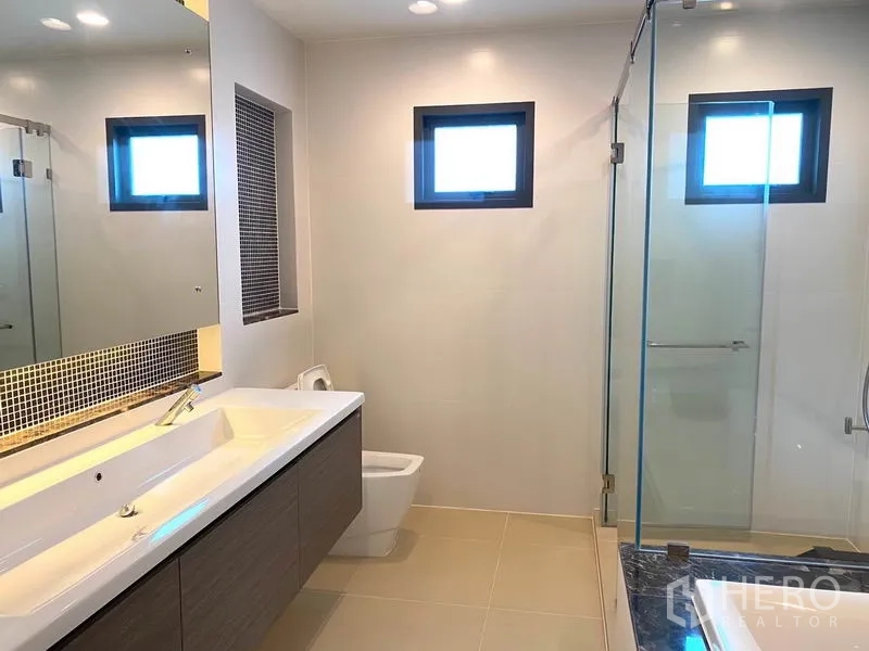 Detached House for rent in Saphan Sung, Bangkok - Bathroom with wide vanity, large mirror, toilet and glass-enclosed shower.