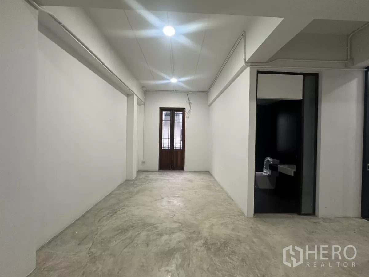 Home Office for rent in Pathum Wan, Bangkok - Long white room with doorway to a black-tiled restroom and a wooden door at the end.