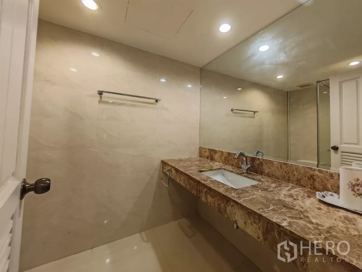 Condominium for rent in Pathum Wan, Bangkok - Bathroom vanity with long marble countertop and wide mirror.
