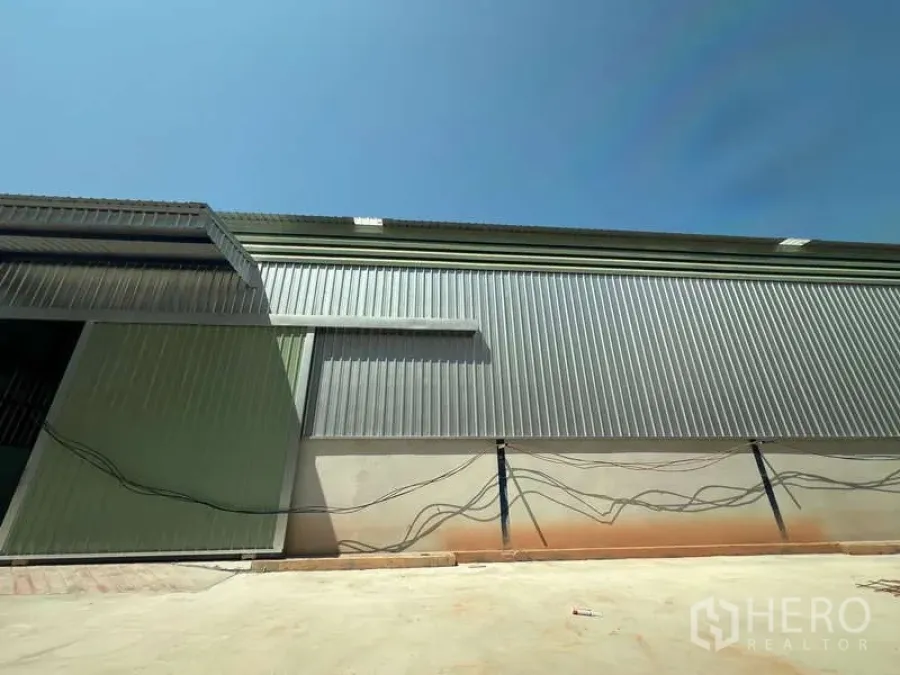 Warehouse for rent in Lat Krabang, Bangkok - Corrugated metal warehouse exterior wall with paved loading apron and utility conduits.