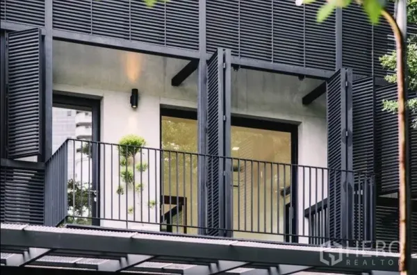 Townhouse for rent in Khlong Toei, Bangkok - Upper-floor balcony with black metal louvers and full-height windows.