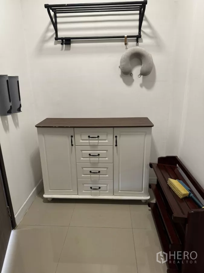 Townhouse for rent in Suan Luang, Bangkok - Storage corner with white sideboard cabinet, wall-mounted rack, and wooden shoe shelf on tiled flooring.