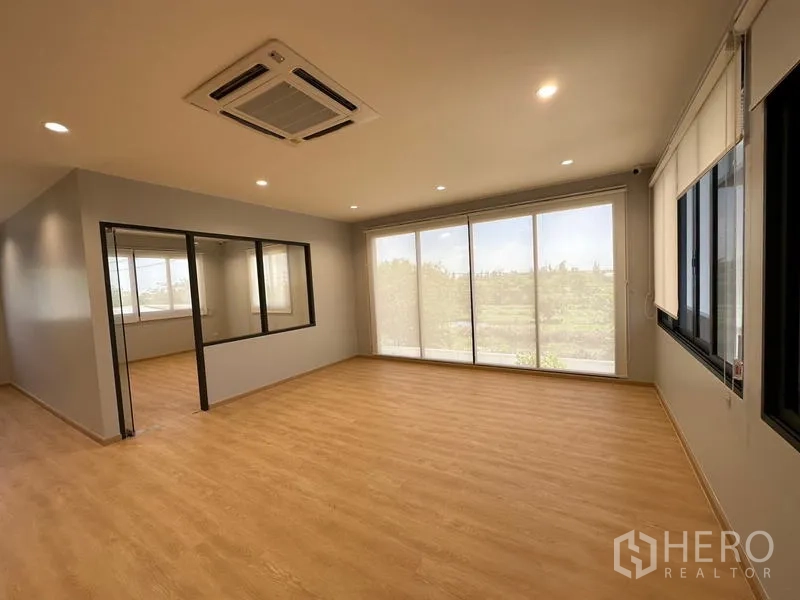 Factory for rent or sale in Lam Luk Ka, Pathum Thani - Corner office with floor‑to‑ceiling windows, cassette air‑conditioner and wood laminate floor.