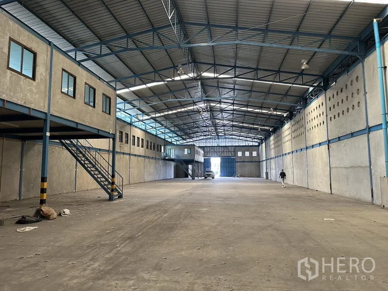 Warehouse for rent in Bang Phli, Samut Prakan - Spacious warehouse interior with high steel truss roof, skylights, and mezzanine offices along one side.