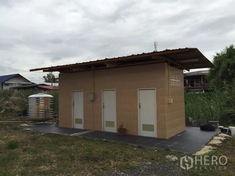 Warehouse for rent in Mueang Pathum Thani, Pathum Thani - Detached restroom block with multiple doors and a stainless water tank on a paved base.