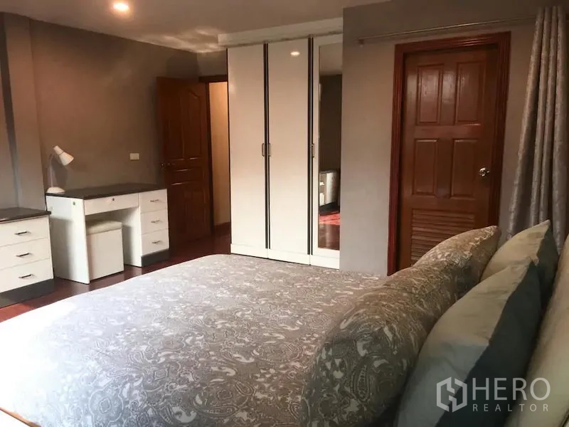 Townhouse for rent in Bang Rak, Bangkok - Bedroom with large bed, white wardrobe, study desk and wooden doors under warm lighting.