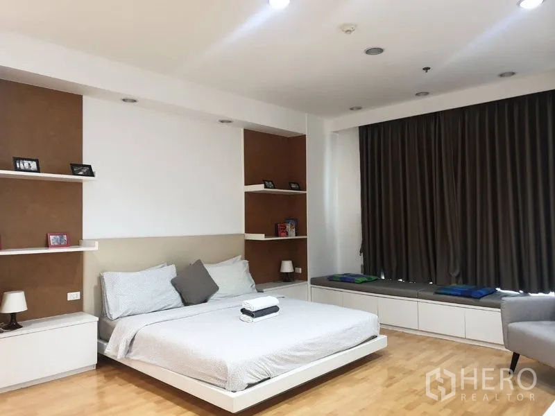 Condominium for rent in Khlong Toei, Bangkok - Master bedroom facing wide windows, TV cabinet, and reading armchair.