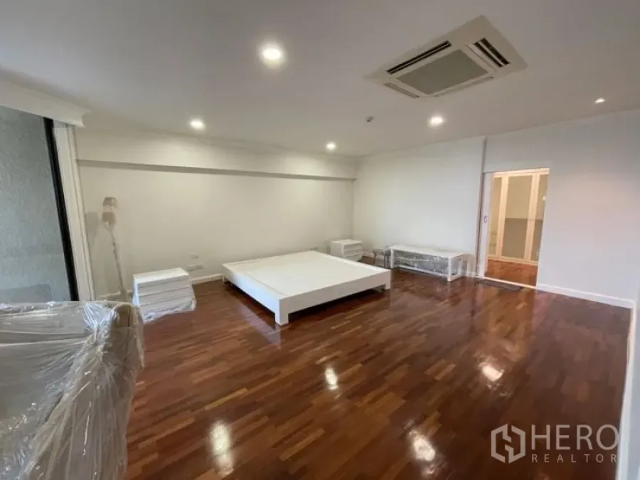 Condominium for rent in Khlong Toei, Bangkok - Large bedroom with platform bed, wood flooring, and sliding glass doors opening to a balcony.