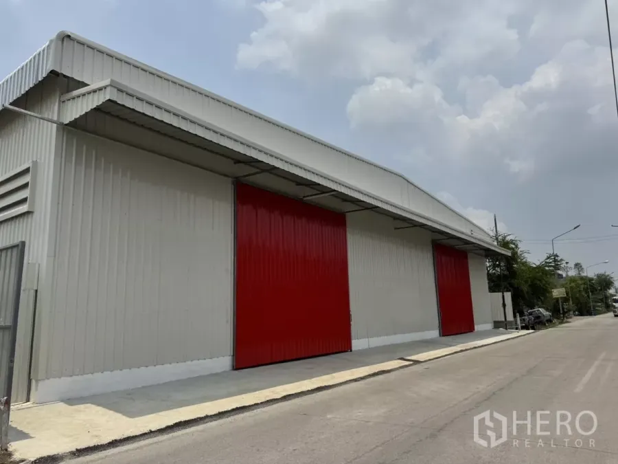 Warehouse for rent in Lam Luk Ka, Pathum Thani - New grey metal warehouse exterior with two oversized red sliding doors on a quiet road in Lam Luk Ka.