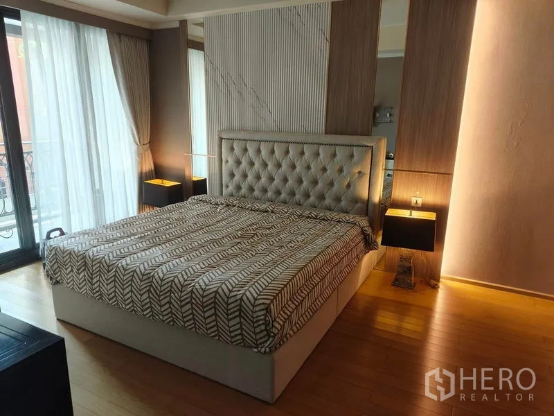 Condominium for rent or sale in Pathum Wan, Bangkok - Master bedroom with tufted bed, accent wall panels, bedside lamps, and wide windows with curtains.