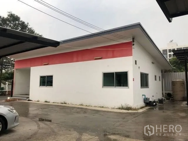 地 出租在Phra Khanong, Bangkok - 单层白色建筑配红色装饰，旁有混凝土院与车棚。