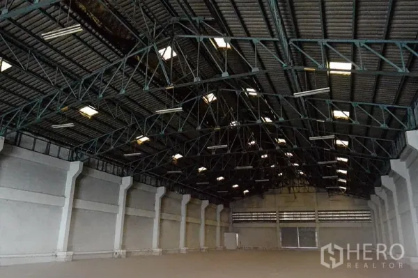 Warehouse for rent in Prawet, Bangkok - Spacious warehouse interior with high steel truss roof, skylights, and smooth concrete floor.