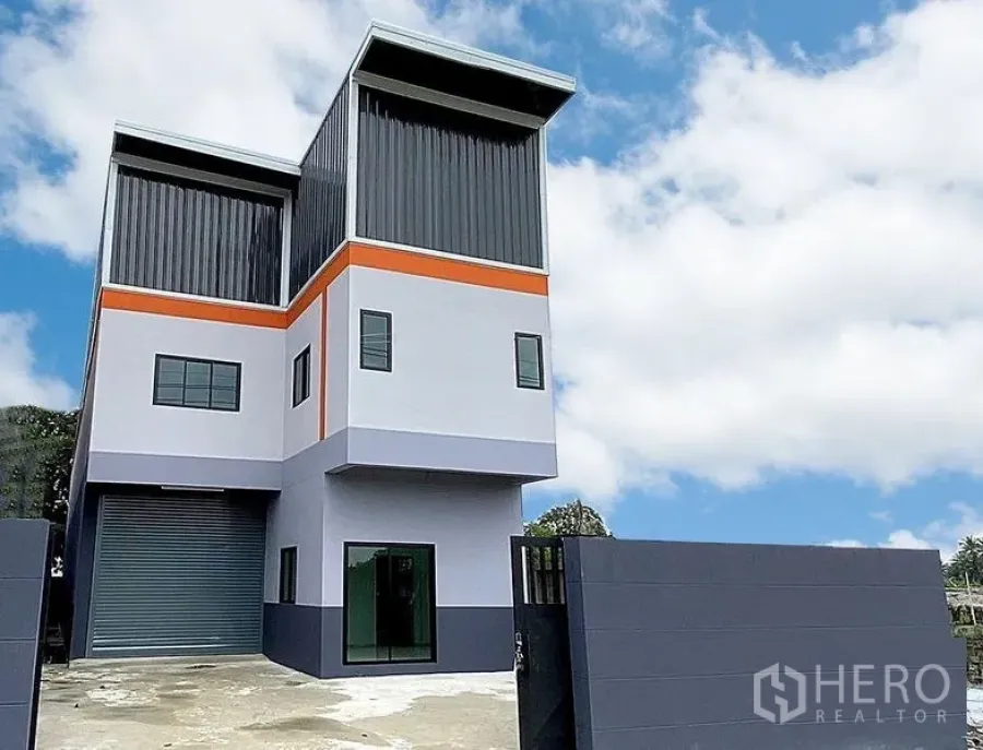 Factory for rent in Bang Bua Thong, Nonthaburi - Modern two-storey factory exterior with roller shutter, gate and parking yard under blue sky in Bang Bua Thong, Nonthaburi.