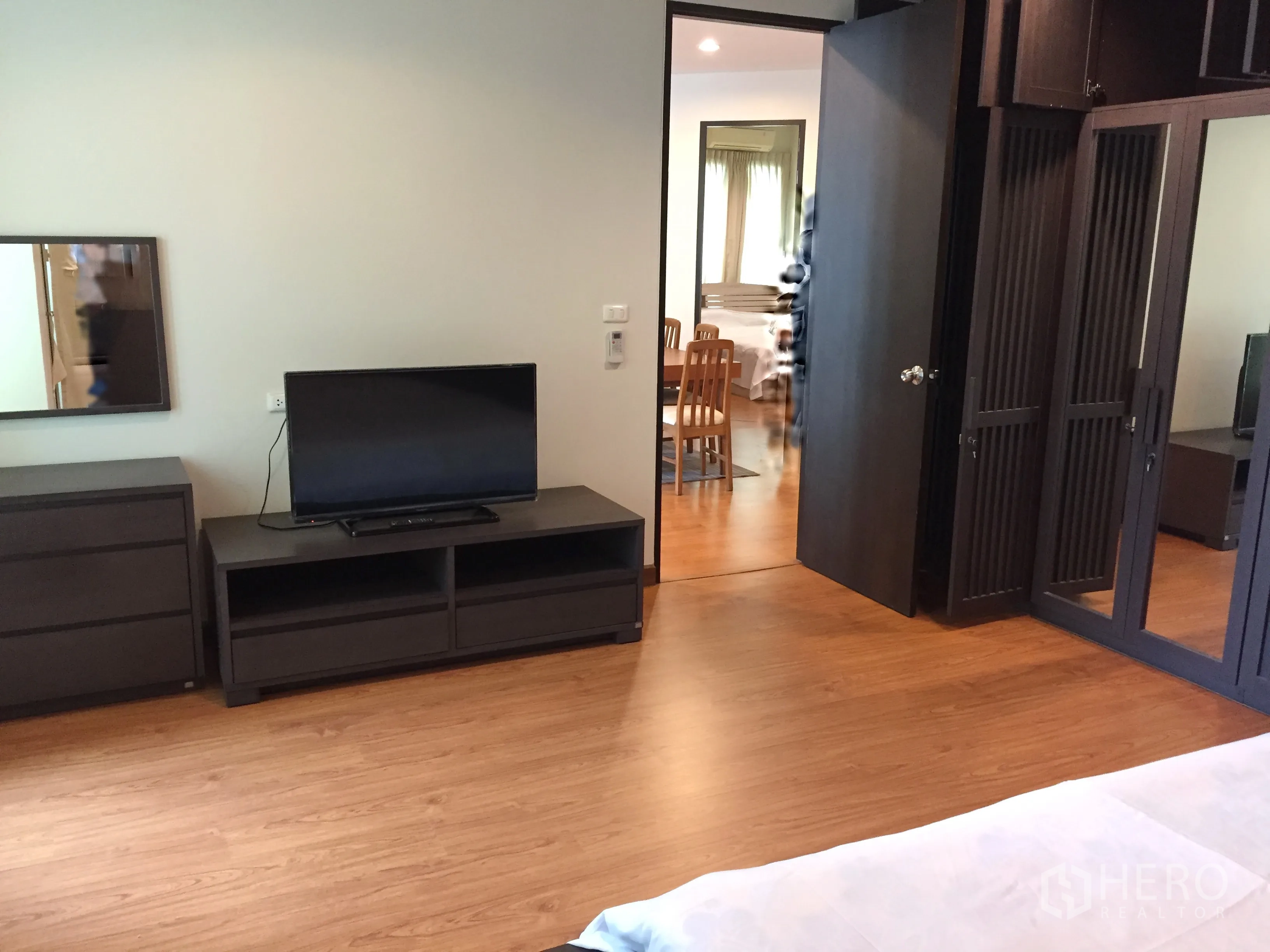 Condominium for rent in Khlong Toei, Bangkok - Spacious master bedroom with TV console, dresser and large wardrobes on wood floors.