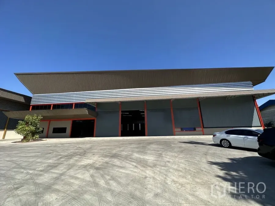 工厂 出租在Chachoengsao - 现代工厂外立面，高挑屋顶、多个卷帘门与宽阔混凝土场地，天空晴朗