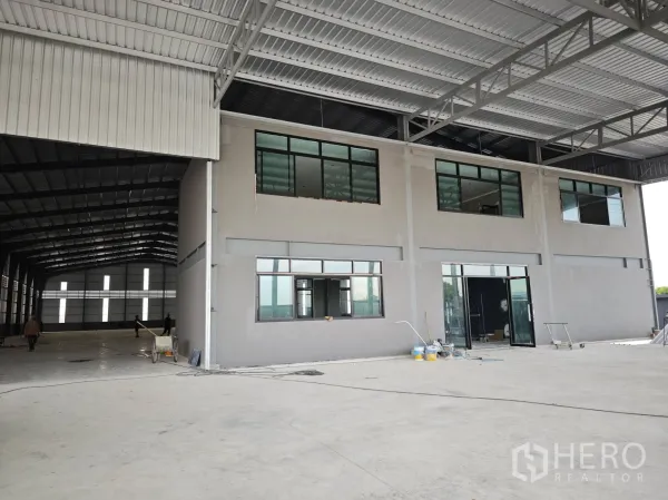 Warehouse for rent or sale in Bang Phli, Samut Prakan - Covered loading area with a two-storey office block and wide concrete floor inside the warehouse.