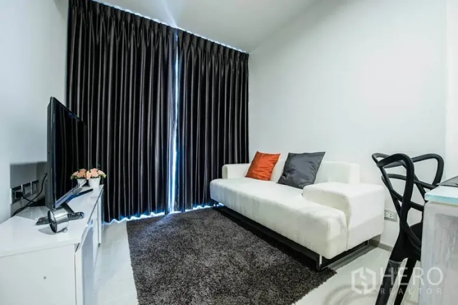 Condominium for rent in Khlong Toei, Bangkok - Modern Ekkamai condo living room with white sofa, TV console and blackout curtains.