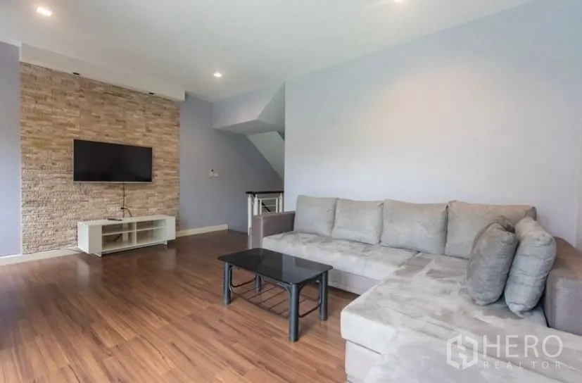 Townhouse for rent in Suan Luang, Bangkok - Another angle of the upper lounge showing grey sectional sofa, wood floors and mounted television.