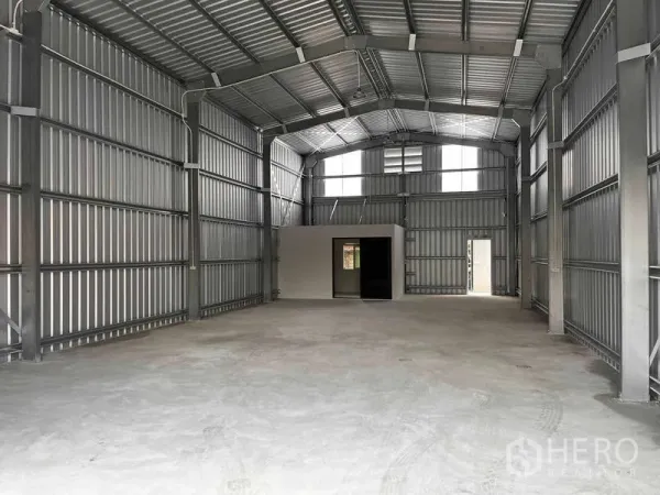 Warehouse for rent in Lat Phrao, Bangkok - Spacious 200 sqm warehouse interior with high steel roof, skylight panels, concrete floor and a small office room with door and window.