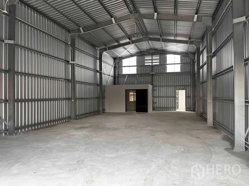 Warehouse for rent in Lat Phrao, Bangkok - Spacious 200 sqm warehouse interior with high steel roof, skylight panels, concrete floor and a small office room with door and window.
