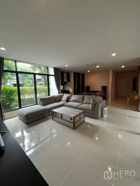Detached House for rent in Bang Kapi, Bangkok - Bright living room with large sectional sofa, floor-to-ceiling windows and glossy tiled floor facing the garden.