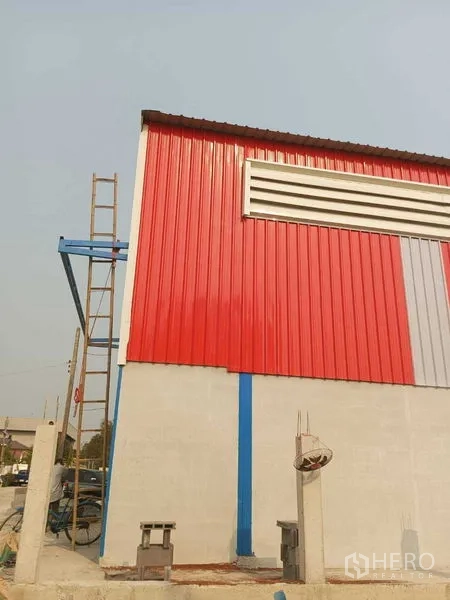 Warehouse for rent in Pathum Thani - Corner view of the warehouse with red metal cladding, ventilation louver, and concrete lower wall.
