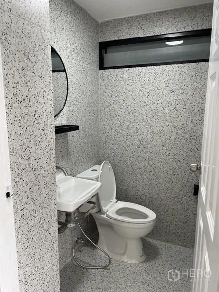 Home Office for rent in Khlong Toei, Bangkok - Compact bathroom with terrazzo-style tiles, round mirror, and white fixtures