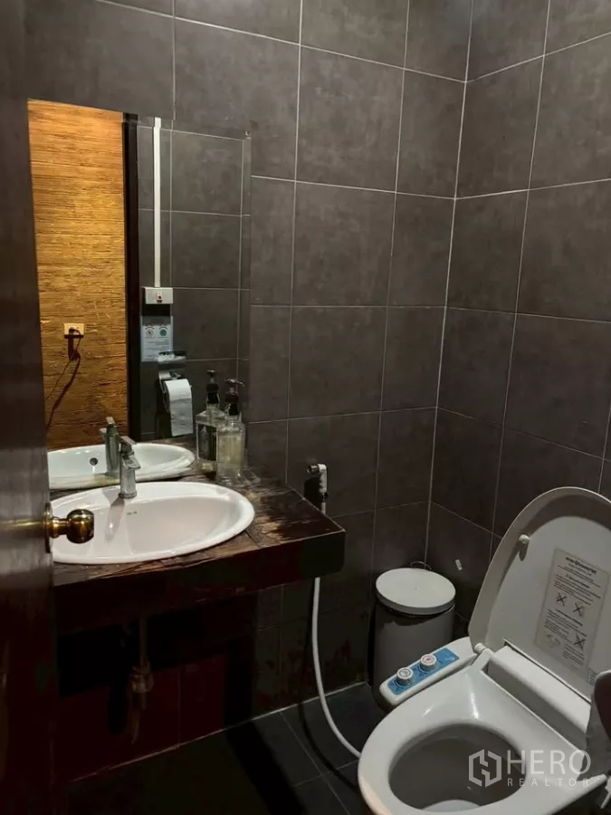 Shophouse for rent in Watthana, Bangkok - Restroom with dark tiles, vanity and bidet toilet.