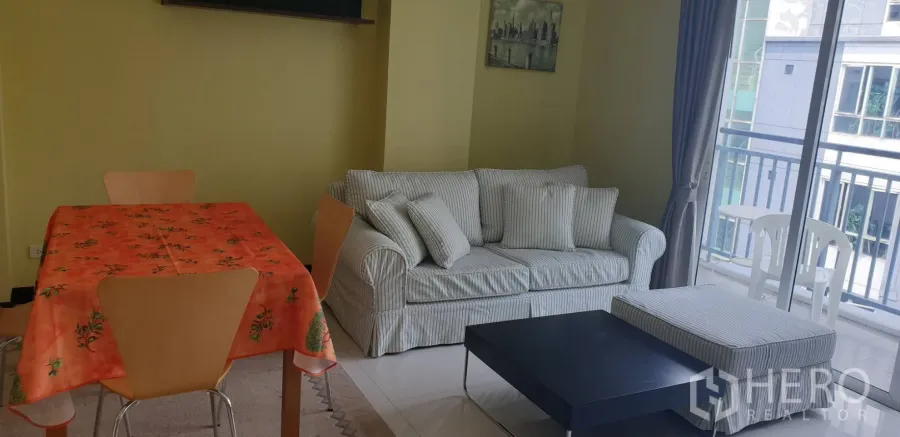 Condominium for rent in Khlong Toei, Bangkok - Living room with striped sofa, dining table, coffee table, and balcony access.