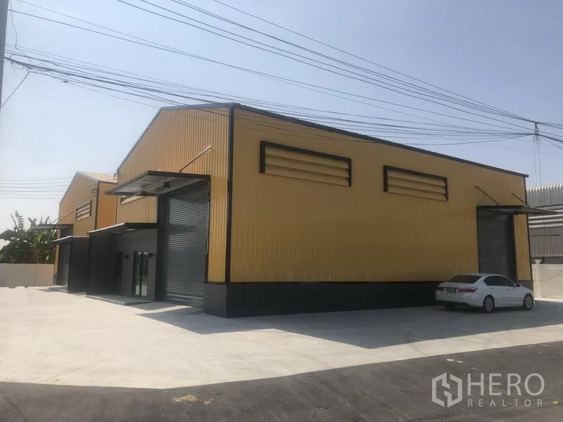 Factory for rent in Bang Yai, Nonthaburi - Side angle of adjoining factory units with louver vents, roller doors and a spacious concrete yard.