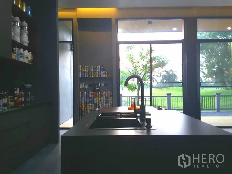 Detached House for rent or sale in Lam Luk Ka, Pathum Thani - Modern island kitchen with double sink facing floor-to-ceiling glass doors and lush green views.